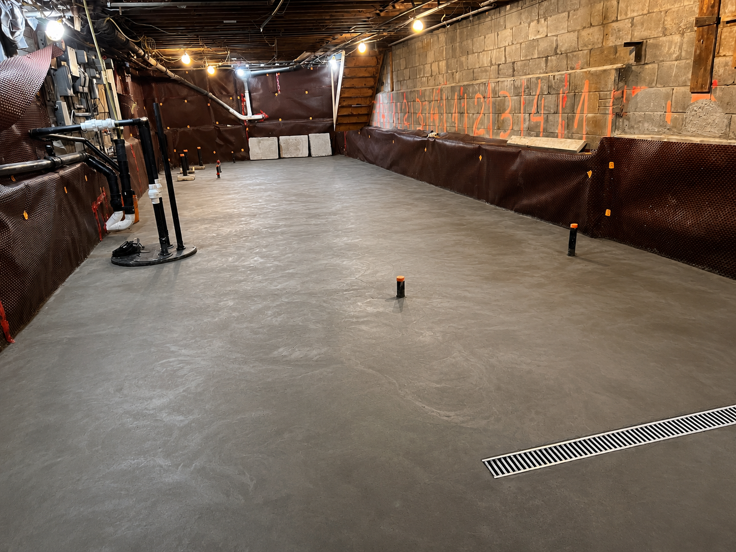 Finished basement underpinning project in North York showing poured concrete floor, new drainage trench, and underpinned foundation wall sections